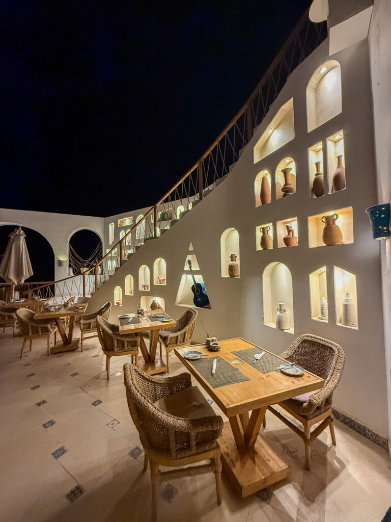 A beautifully designed restaurant at Benben by Dhara in Aswan, featuring warm lighting, whitewashed walls with decorative niches, and wooden furniture creating a cozy ambiance.