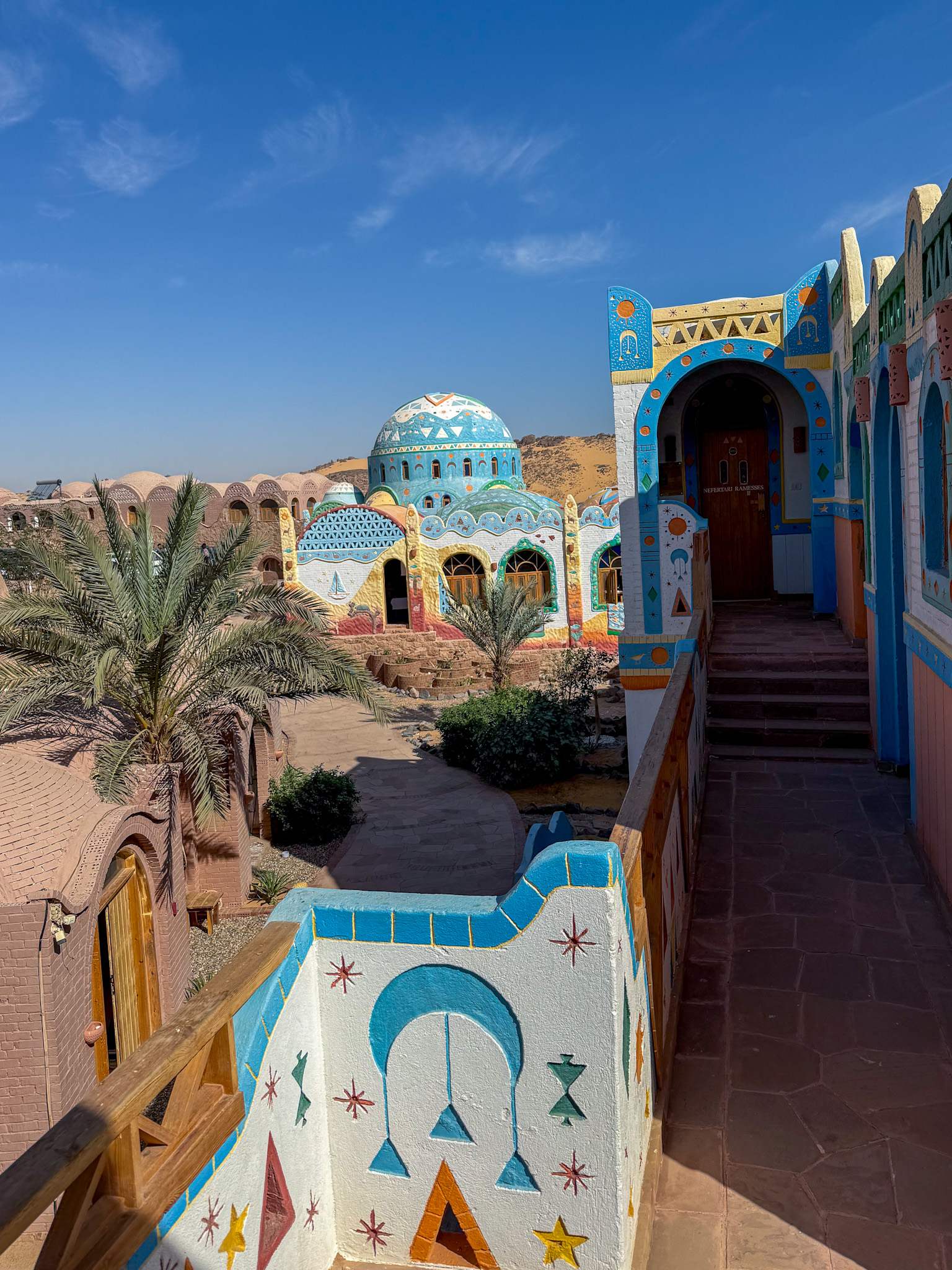 A sunlit pathway leading through the colorful, traditionally painted domes of Kato Dool in Aswan, Egypt.