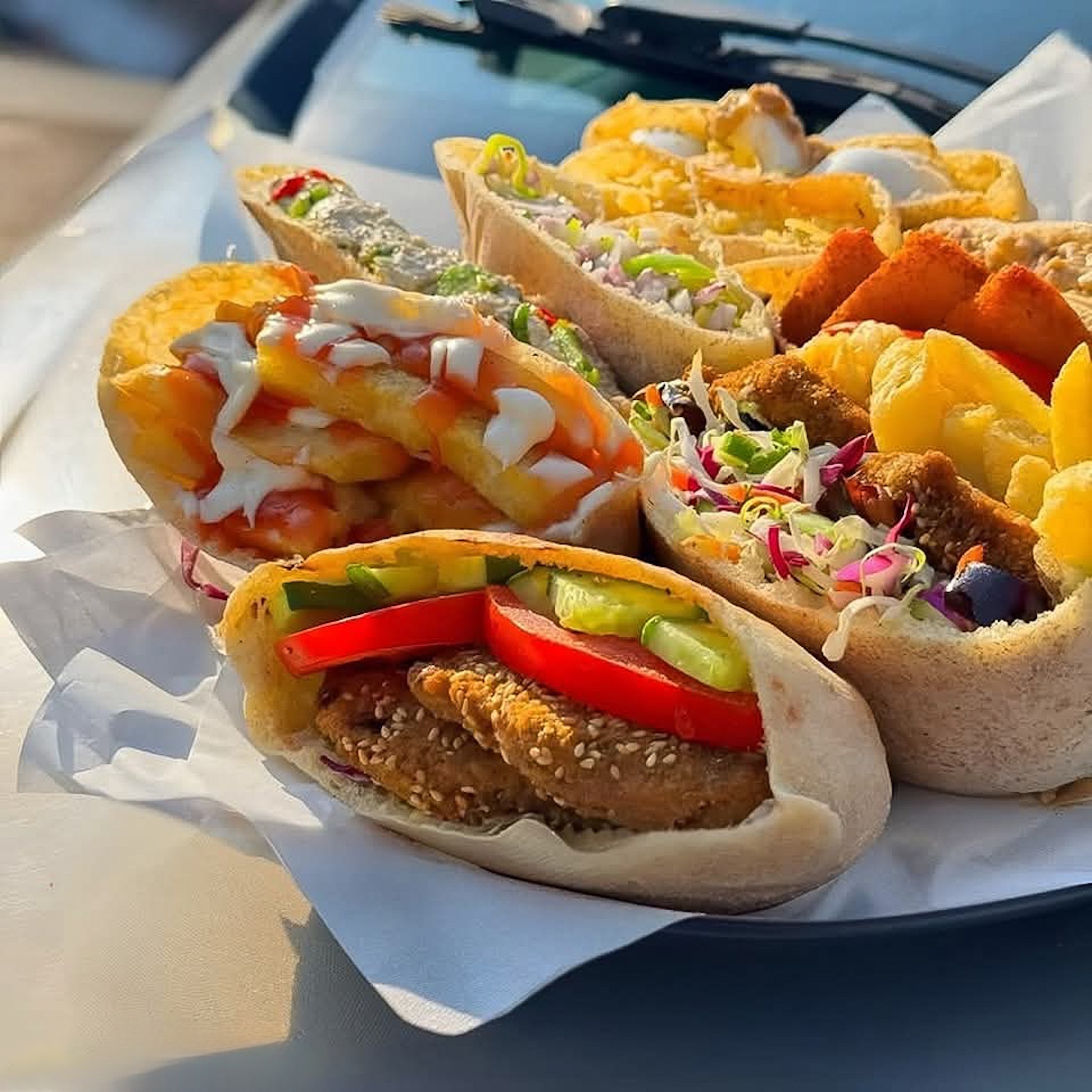 A close-up of freshly made falafel sandwiches filled with crispy falafel, fresh vegetables, fries, and drizzled with sauces, served on a tray in Luxor, Egypt.