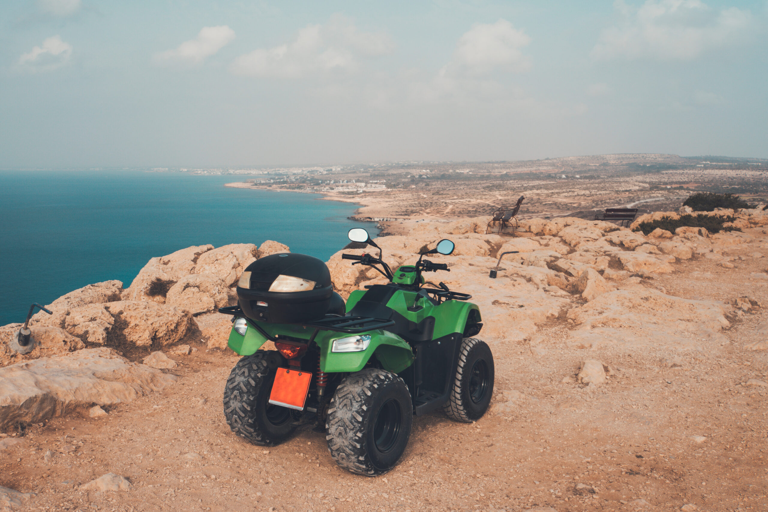 Green quad bike parked on a rocky cliff overlooking the coastline of Ayia Napa, Cyprus, with stunning sea views in the background.