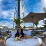 A woman relaxing on a sunbed at a luxury beach club with the iconic Burj Al Arab in Dubai towering in the background.