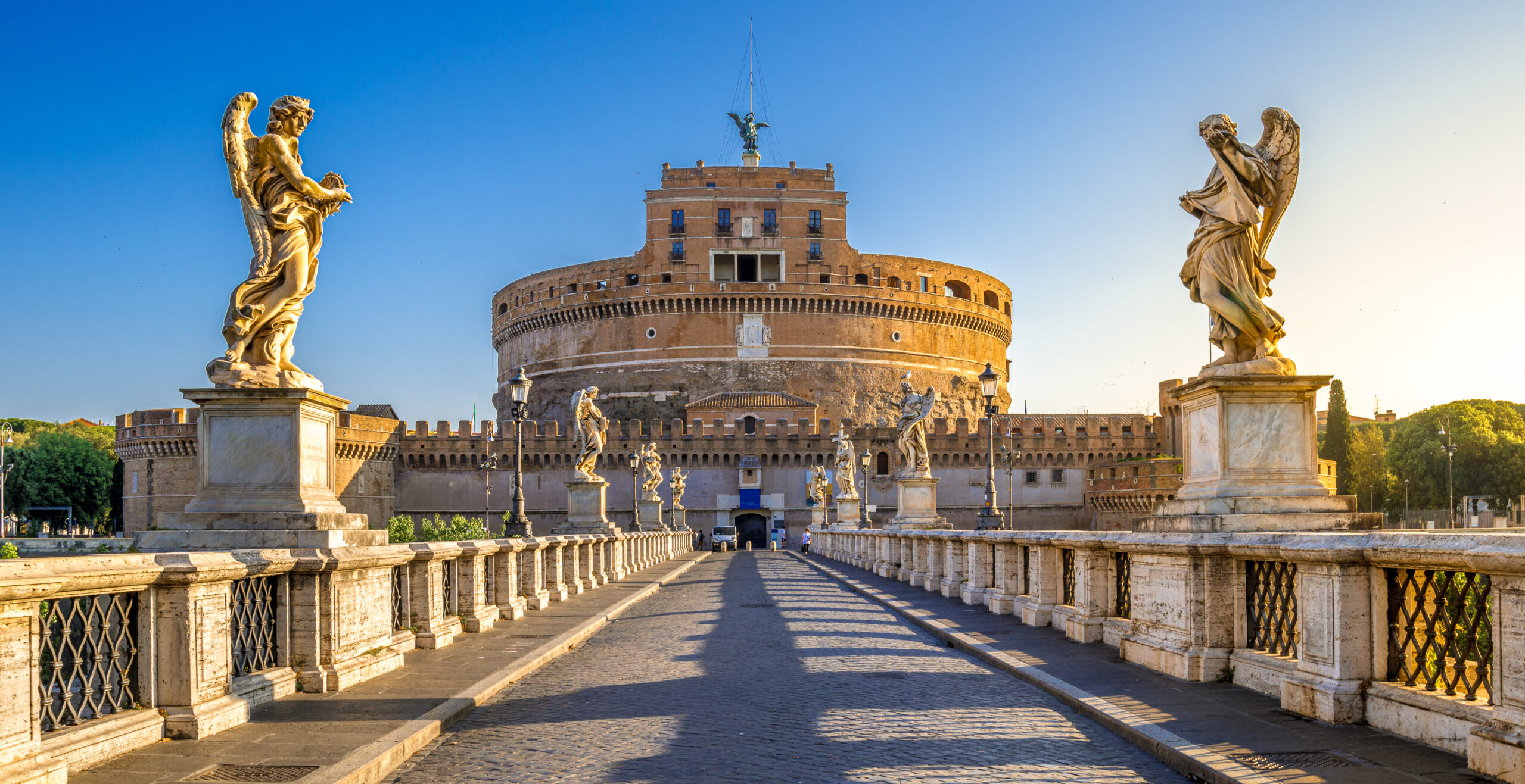 Castel Sant’Angelo in Rome with Ponte Sant’Angelo bridge leading to the historic fortress, framed by angel statues and bathed in warm sunlight