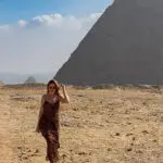 A traveler exploring the Giza Pyramids in Egypt, one of the Seven Wonders of the Ancient World, under a clear blue sky.