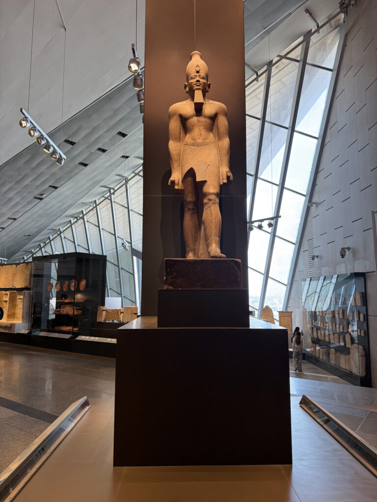 A towering statue of an ancient Egyptian pharaoh at the Grand Egyptian Museum in Giza, surrounded by modern architectural design.