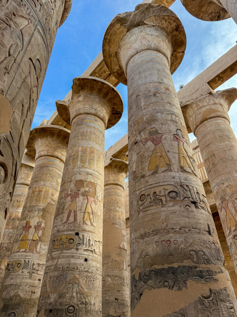 Towering ancient columns of Karnak Temple, covered in intricate hieroglyphs, standing against a bright blue sky in Luxor, Egypt.