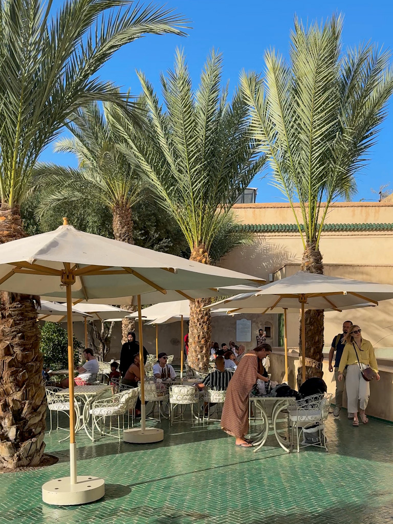 The peaceful courtyard café at Le Jardin Secret in Marrakech, surrounded by lush palm trees and traditional Moroccan architecture.