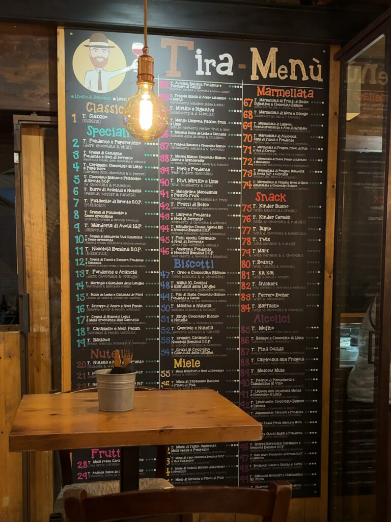 A menu board at Mr. 100 Tiramisu in Rome, showcasing over 100 flavors of tiramisu, with a cozy wooden table in the foreground.