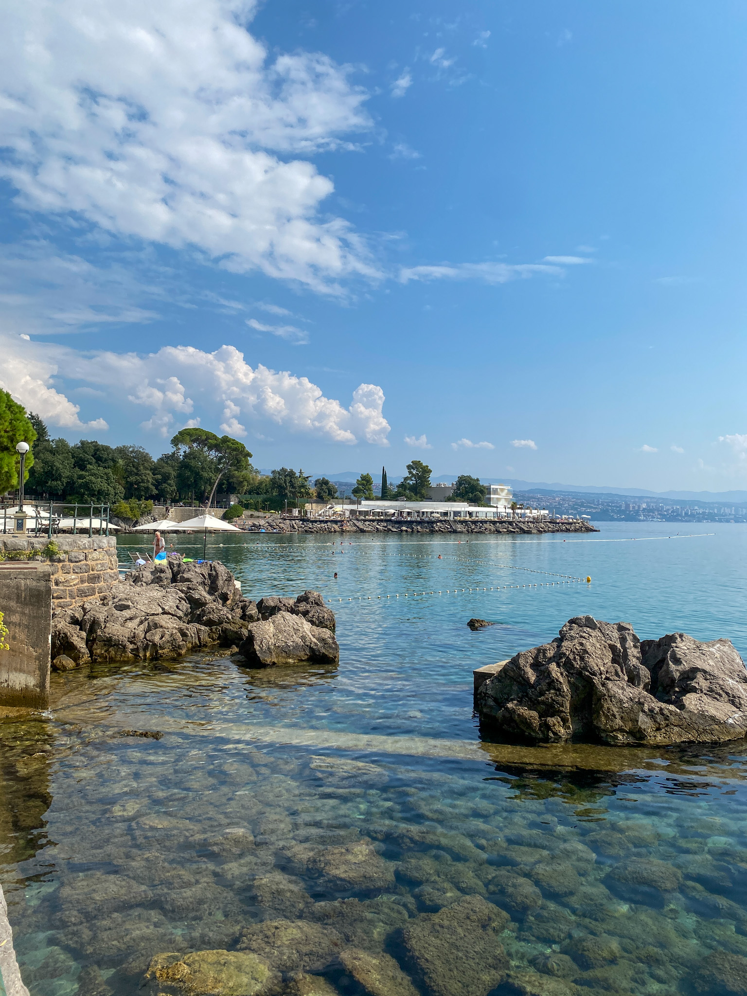 Scenic view of Opatija’s promenade with crystal-clear Adriatic waters, rocky coastline, and a luxury beach club in the distance.