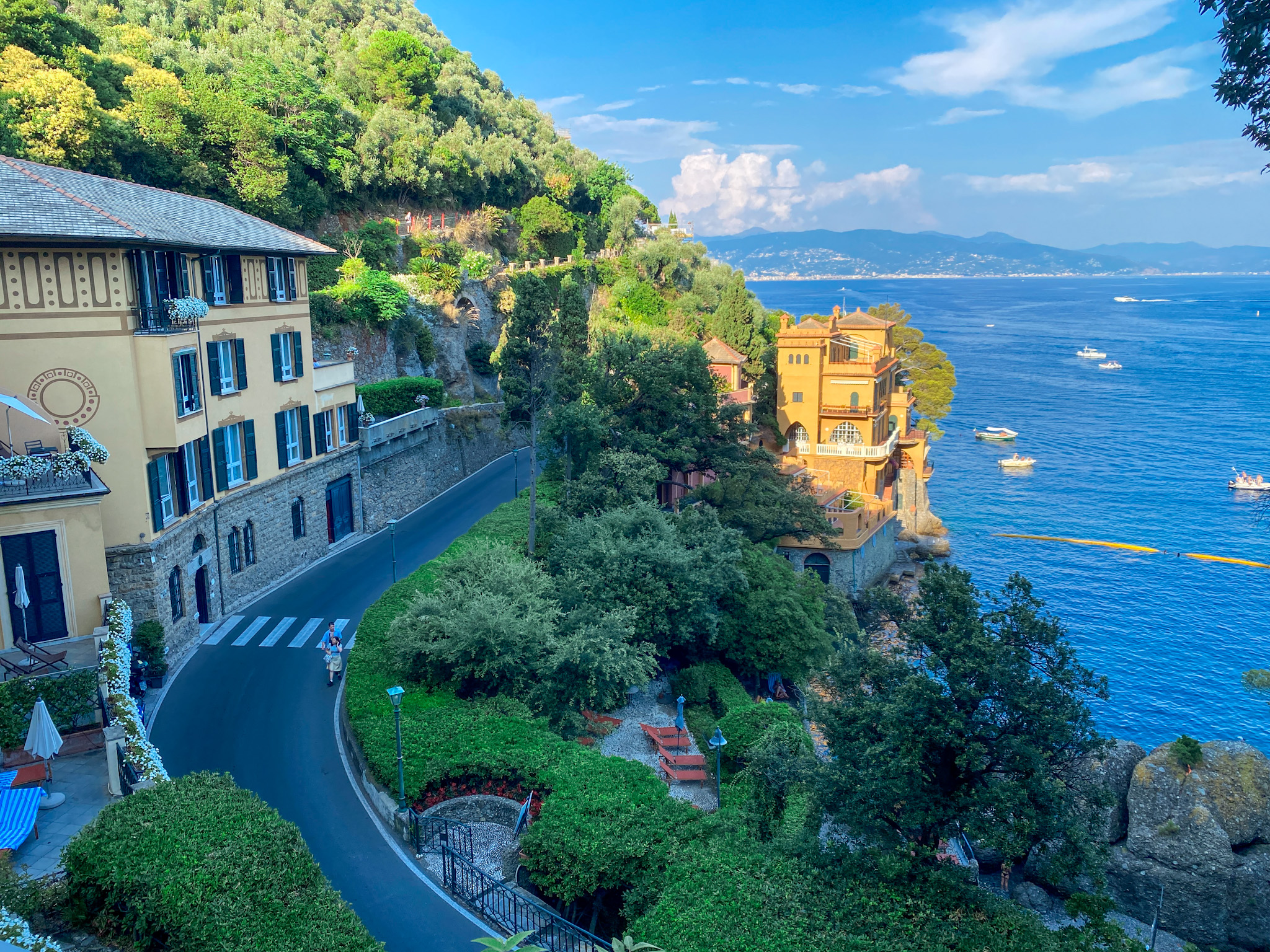 A stunning view of the winding coastal road leading to Portofino, with elegant Italian villas, lush greenery, and the sparkling blue Ligurian Sea in the background.