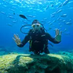 Standing at the edge of a scenic sea cave in Ayia Napa, Cyprus, overlooking the turquoise blue Mediterranean waters with limestone cliffs in the background.