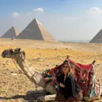 Woman posing with a camel in front of the Giza Pyramids in Egypt.