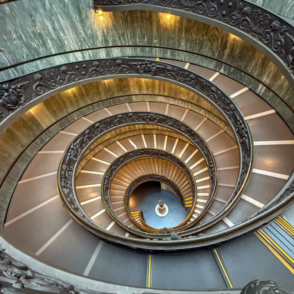 A mesmerizing spiral staircase inside the Vatican Museums is designed with intricate railings and a grand architectural style.