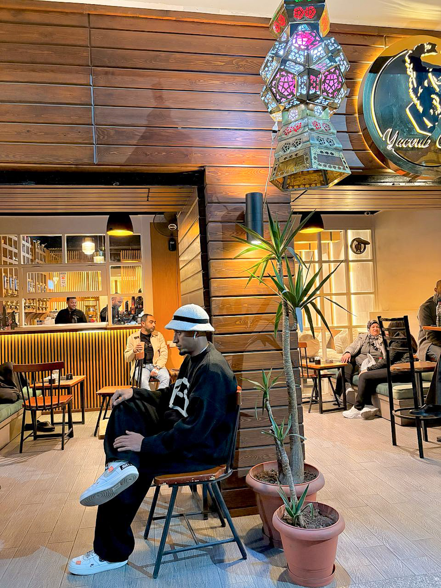 Man sitting outside Yacoub Coffee in Luxor, Egypt, surrounded by traditional lanterns and plants, enjoying the relaxed local café atmosphere in the evening.