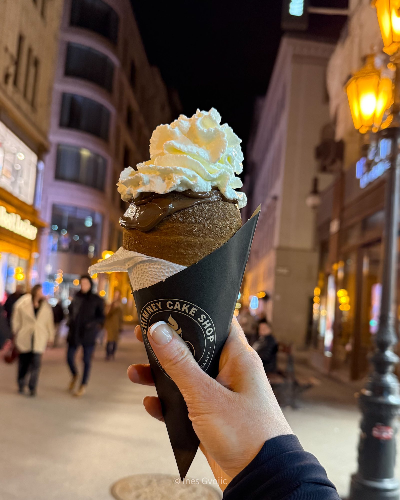 Hand holding a chimney cake topped with Nutella and cream in Budapest at night