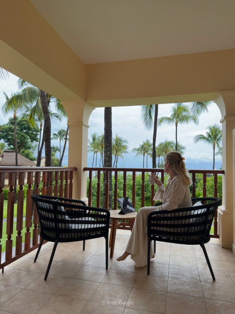 Woman having coffee on balcony with ocean and palm tree view at Hilton Mauritius Resort.