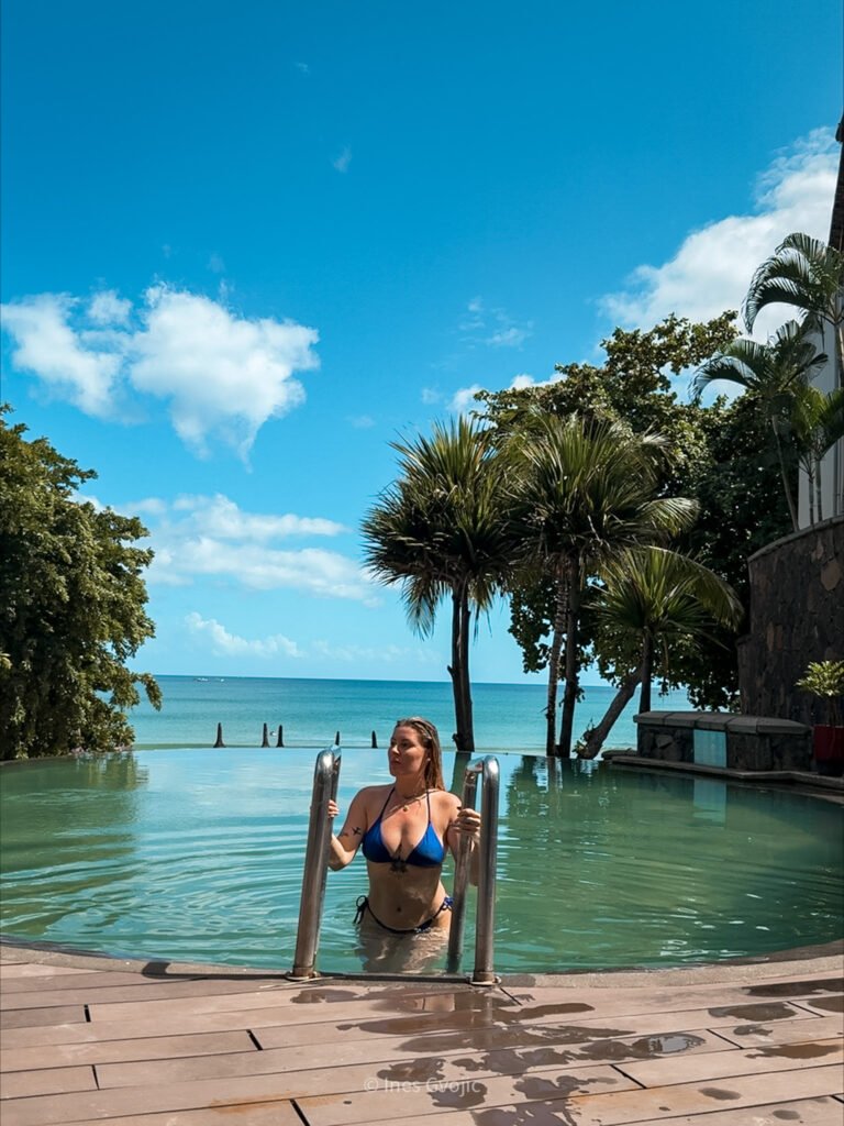 Woman at Tamarina Golf Hotel infinity pool with ocean view and tropical palm trees in Mauritius.