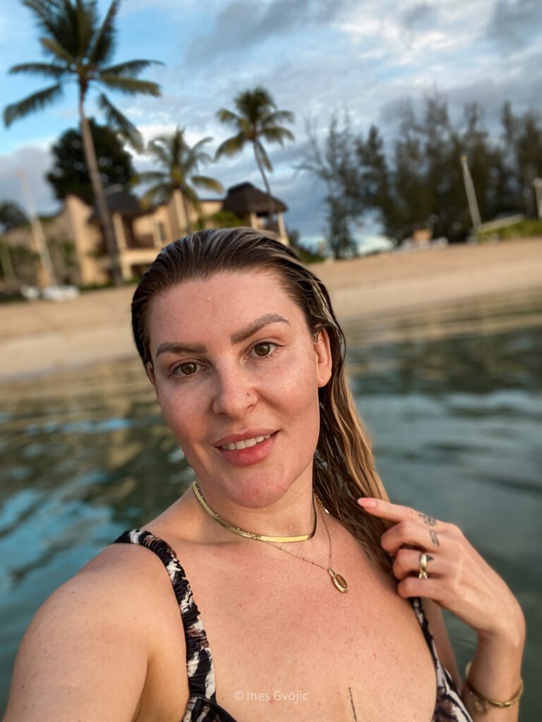 Woman taking a selfie while swimming at sunset on a tropical Mauritius beach with palm trees behind.