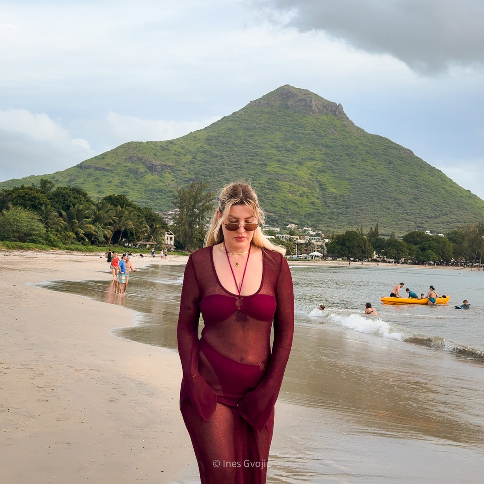 Woman in burgundy swimwear walking along Tamarina Beach with green mountain in the background, Mauritius.