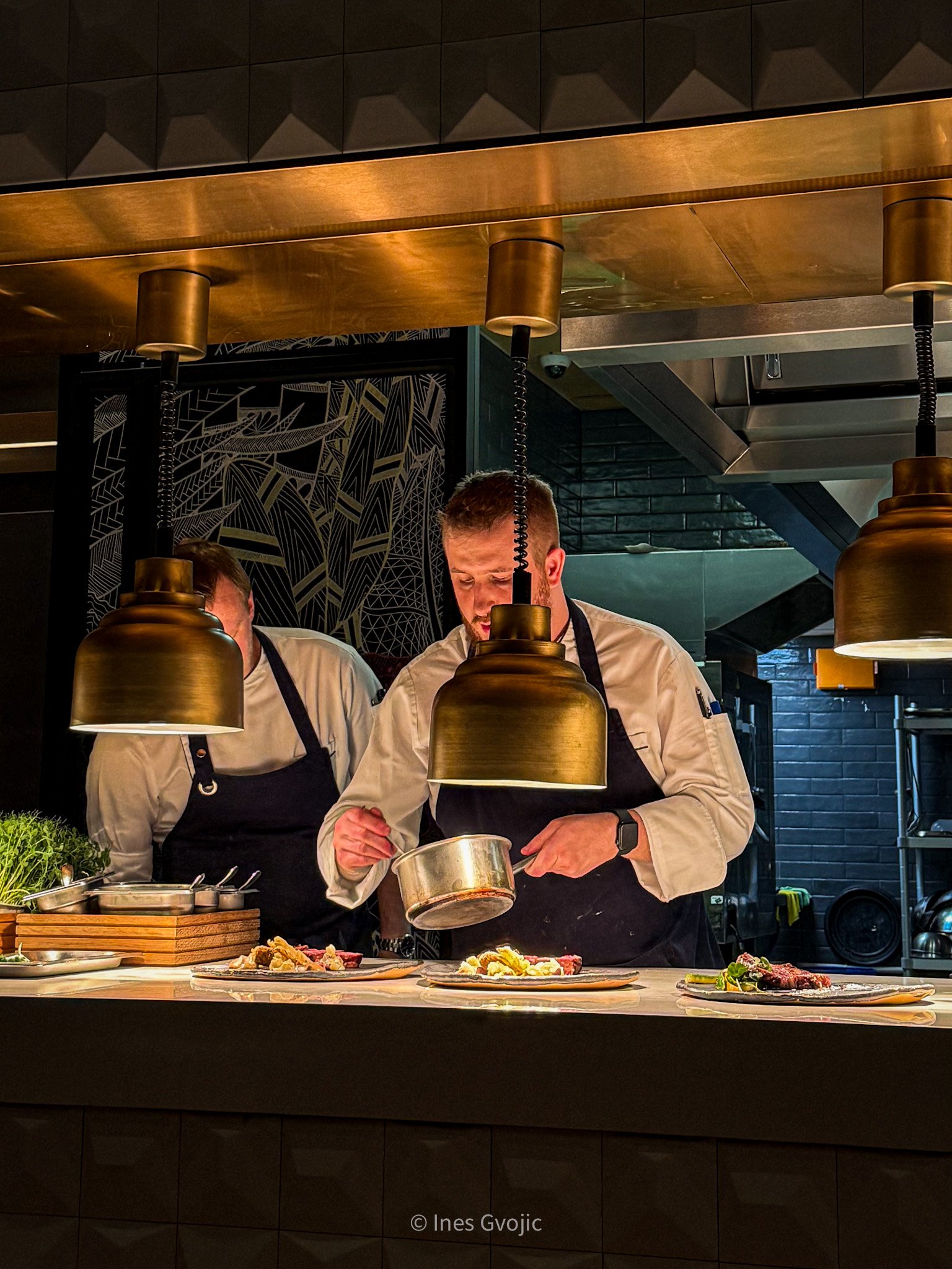 Chefs preparing food at Spago Budapest's open kitchen under golden pendant lights
