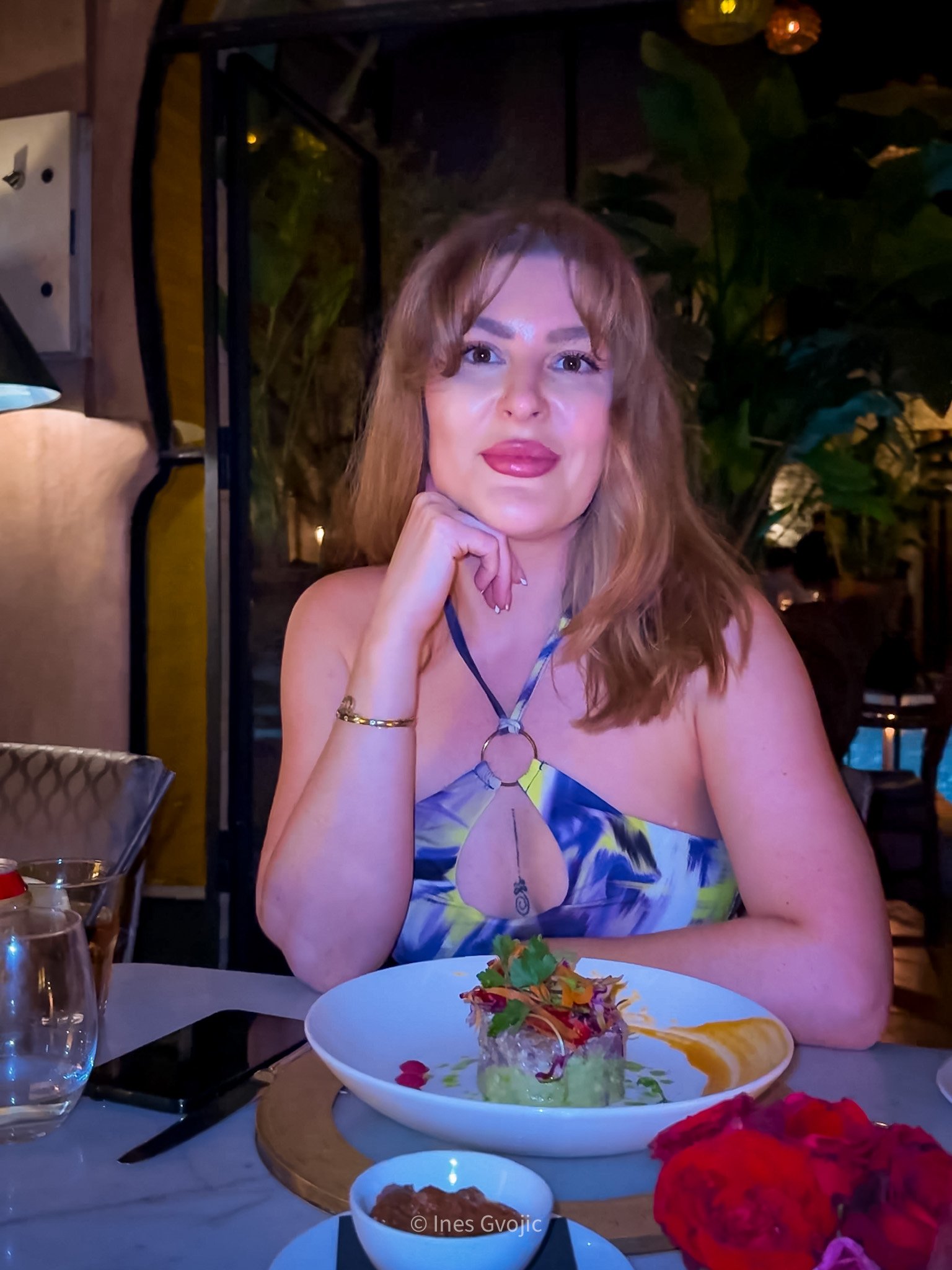 Woman in a patterned dress dining at La Trattoria in Marrakech with gourmet food and roses on the table.