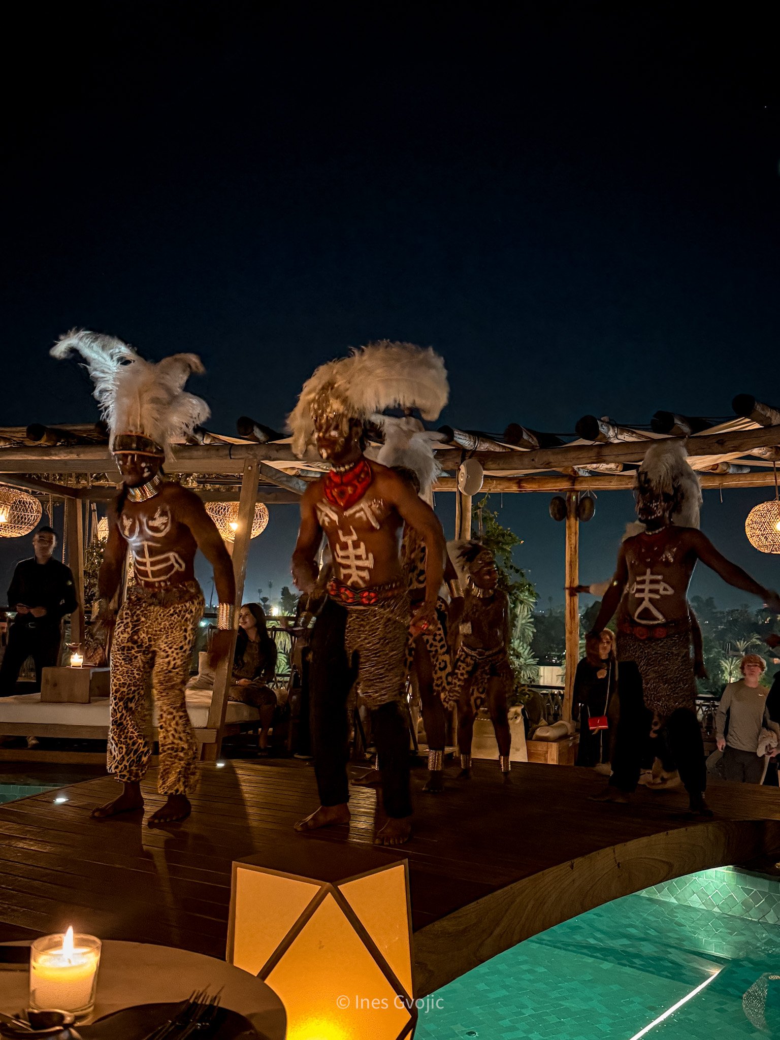 Traditional performers dancing on a wooden stage above a lit pool at Nobu Marrakech, surrounded by candlelight and guests.