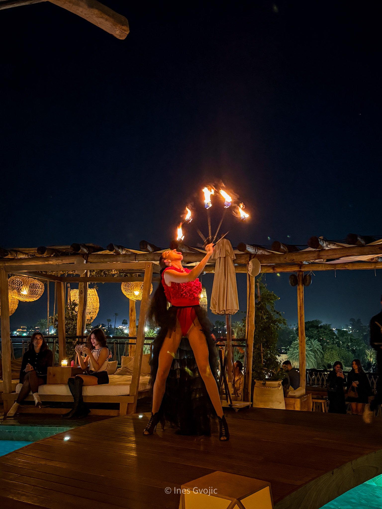 Performer in red costume spinning fire torches on a rooftop stage at Nobu Marrakech, with guests seated nearby under ambient lighting.