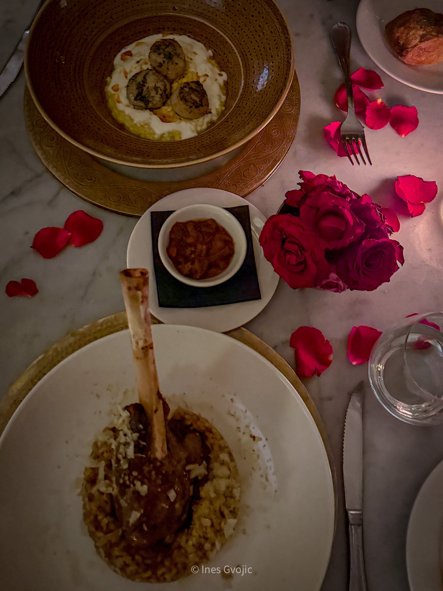 Lamb shoulder dish and scallop appetizer on a marble table with rose petals and red roses at La Trattoria Marrakech.