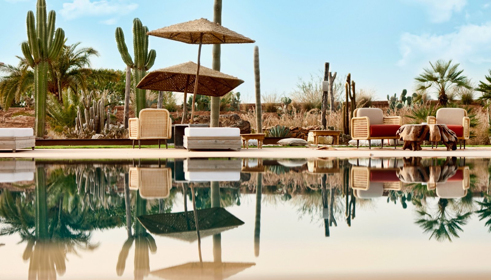 Outdoor resort seating area with umbrellas and a pool, surrounded by cactuses and desert landscaping near Marrakech, Morocco.