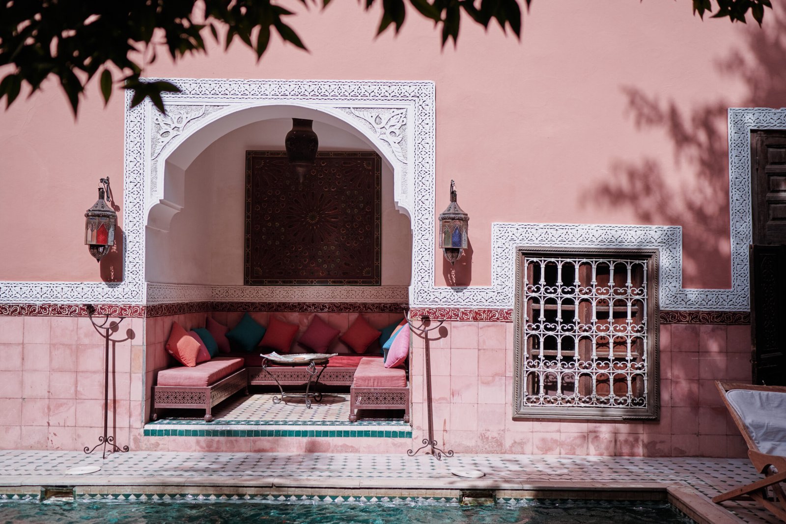 Traditional Moroccan riad courtyard with a pink wall, arched seating area, and decorative pool in Marrakech.