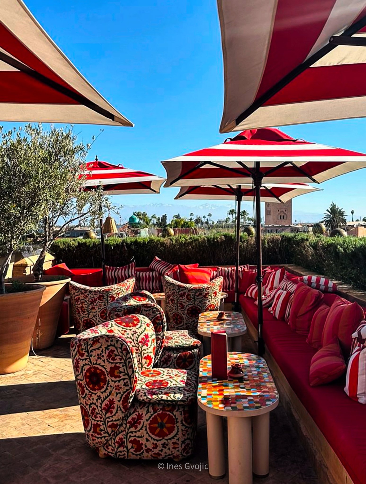 Colourful rooftop lounge at El Fenn Marrakech with red umbrellas and patterned chairs.