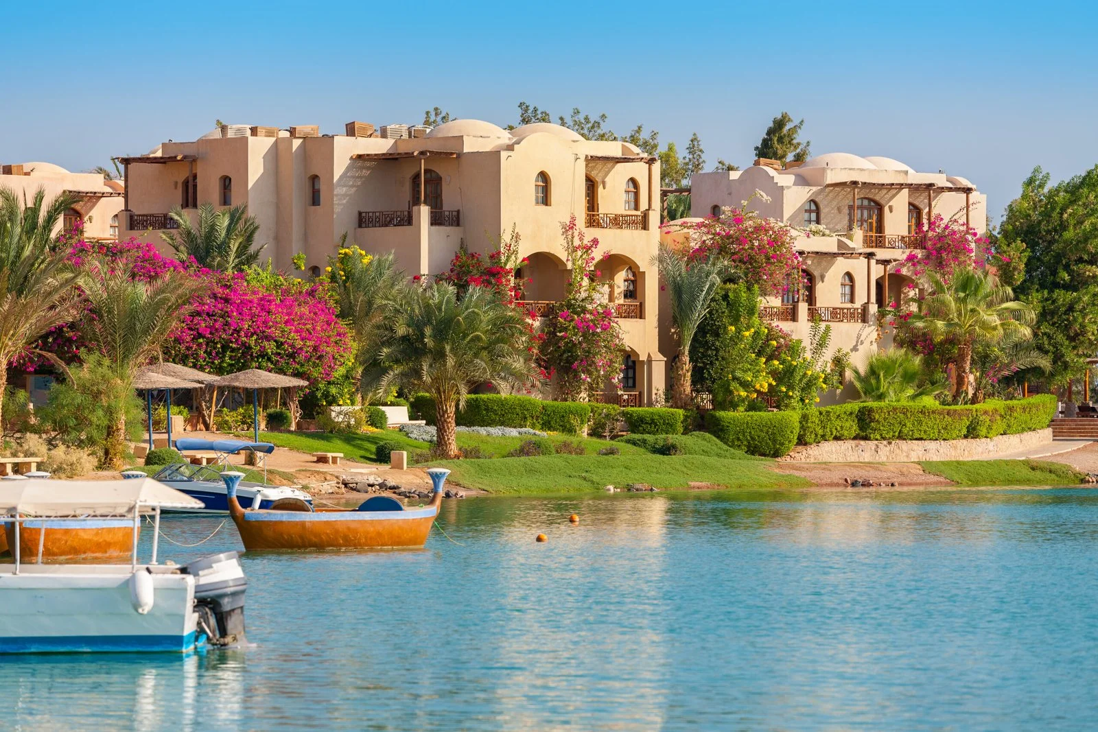 Lagoon view in El Gouna with boats on the water, traditional beige villas, and lush greenery with pink bougainvillea.
