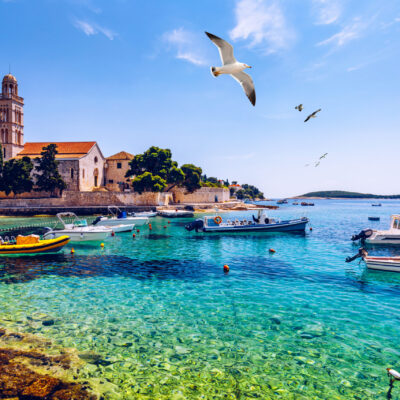 Crystal-clear waters of Hvar, Croatia, with boats floating near the historic Franciscan Monastery.