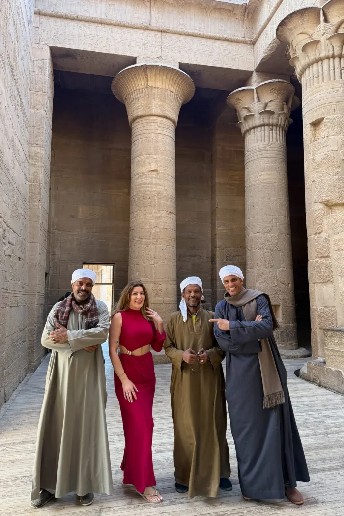 Philae Temple in Aswan, Egypt, featuring ancient Egyptian columns and carvings, with a traveler in a red dress posing with local Nubian men.