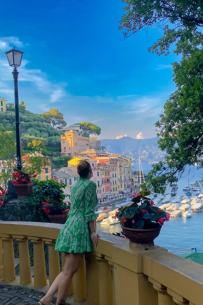 A woman in a green dress admiring the stunning Portofino harbor from a scenic viewpoint, with colorful buildings and yachts in the background.