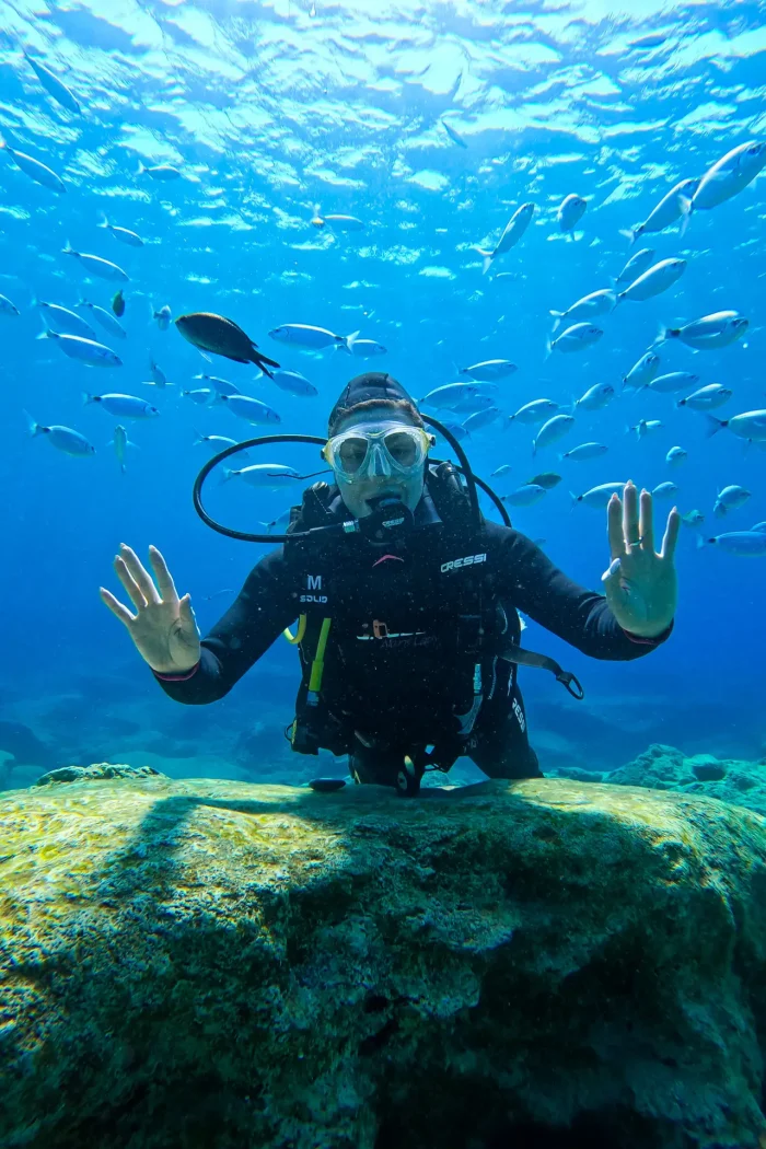 Standing at the edge of a scenic sea cave in Ayia Napa, Cyprus, overlooking the turquoise blue Mediterranean waters with limestone cliffs in the background.